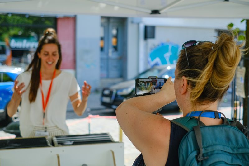 Eine Frau erklärt ein Exponat der Singbusausstellung, eine andere Frau filmt sie mit dem Handy.